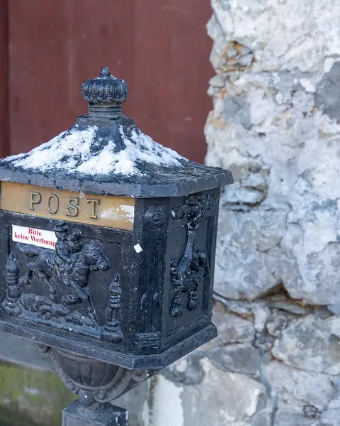Une ancienne boîte aux lettres en fonte, couverte de neige, devant un mur de pierre à Werdenberg.