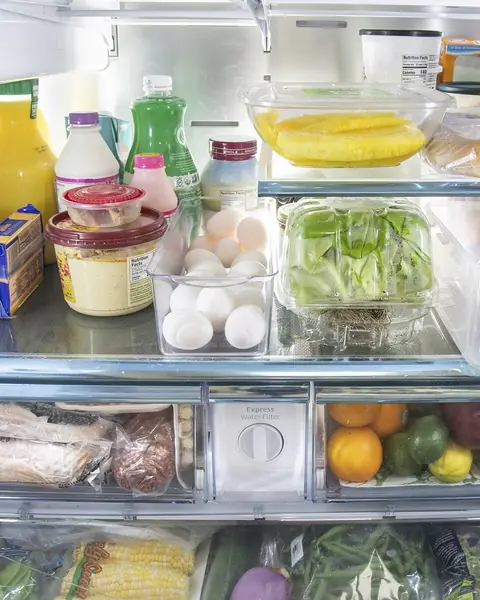 Intérieur d'un réfrigérateur rangé : bouteilles, œufs, salade, bacs à légumes du réfrigérateur en bas.
